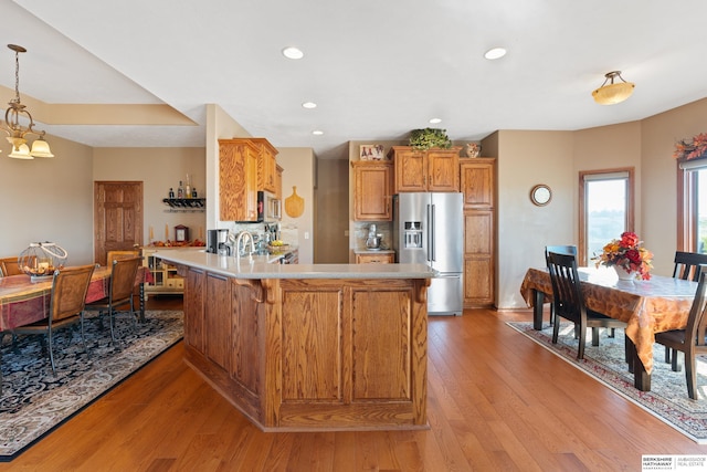 kitchen with brown cabinets, light wood-style flooring, a peninsula, appliances with stainless steel finishes, and light countertops