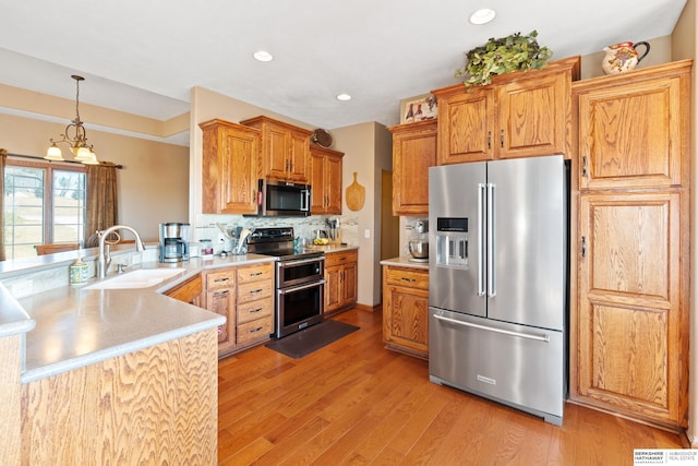 kitchen featuring a peninsula, light wood-style flooring, a sink, stainless steel appliances, and light countertops