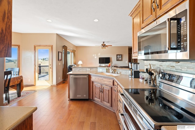 kitchen featuring a ceiling fan, a sink, light wood-style floors, appliances with stainless steel finishes, and a peninsula