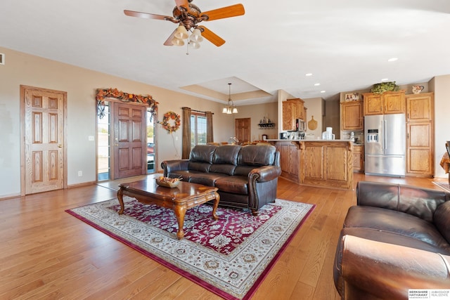 living room featuring baseboards, a tray ceiling, light wood-style flooring, recessed lighting, and ceiling fan