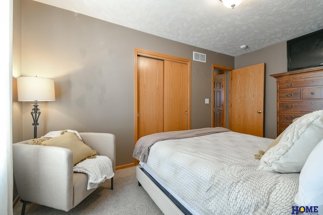 carpeted bedroom featuring a closet, a textured ceiling, and visible vents