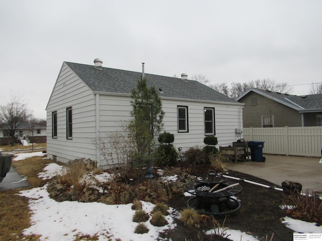 snow covered back of property with a patio area, fence, and roof with shingles