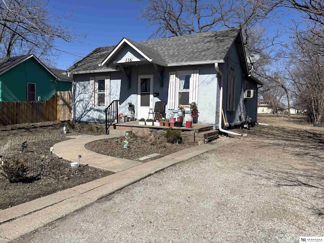 bungalow-style home featuring stucco siding, roof with shingles, and fence