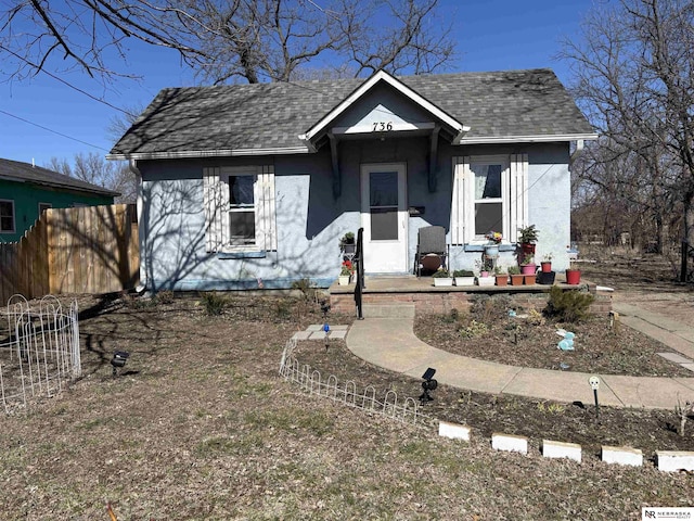 bungalow featuring fence, roof with shingles, and stucco siding