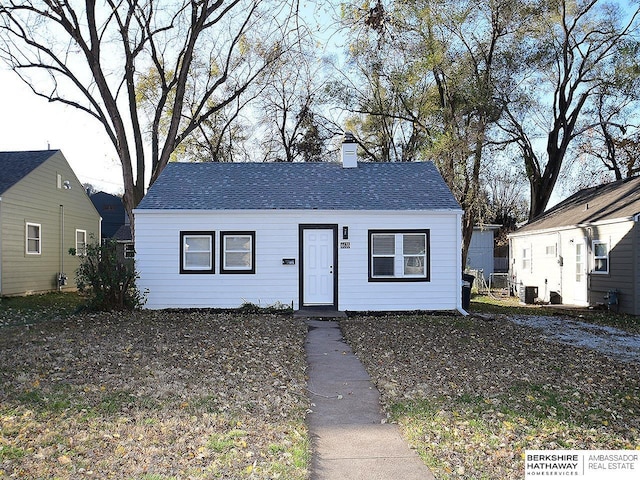 bungalow-style house with roof with shingles, central AC, and a chimney