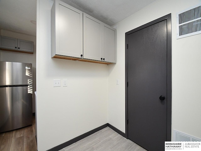 clothes washing area with baseboards, visible vents, light wood finished floors, and a textured ceiling