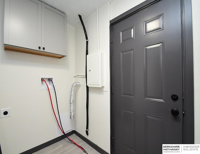 laundry room featuring baseboards, hookup for a washing machine, light wood-style flooring, cabinet space, and a textured ceiling