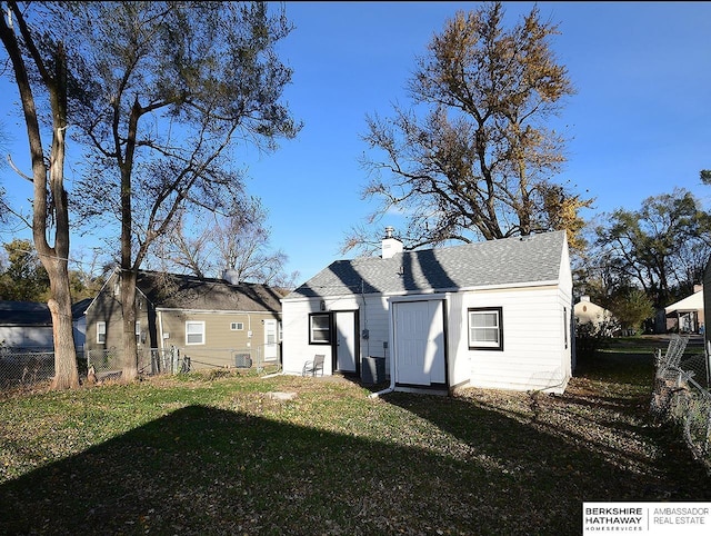 rear view of house featuring central air condition unit, fence, a yard, roof with shingles, and a chimney