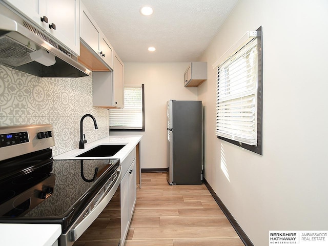 kitchen featuring backsplash, under cabinet range hood, appliances with stainless steel finishes, light wood-style floors, and a sink