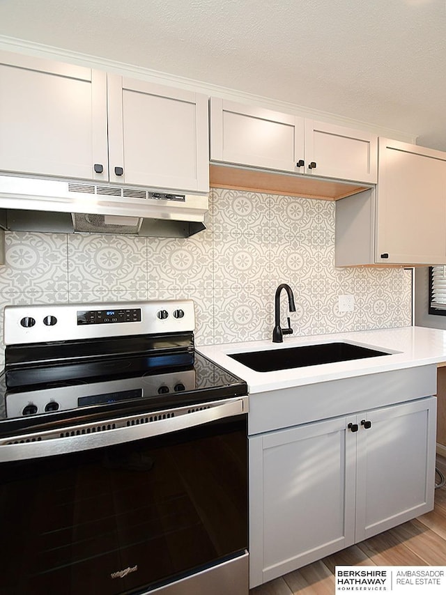 kitchen with under cabinet range hood, a sink, tasteful backsplash, stainless steel electric range, and light countertops