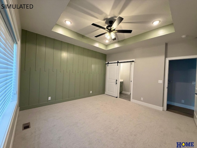 unfurnished bedroom with visible vents, carpet, a raised ceiling, and a barn door