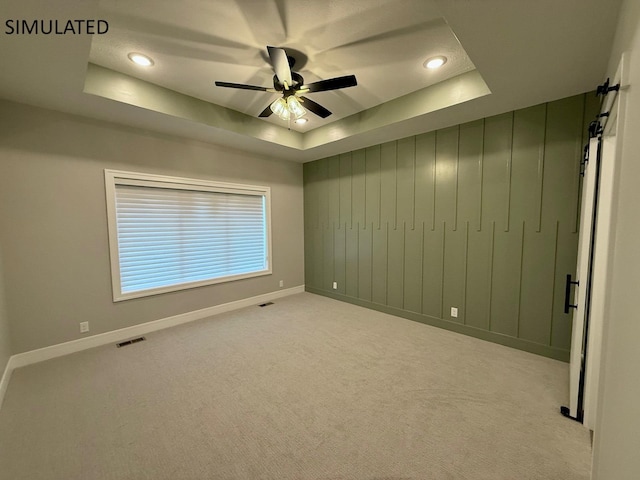 carpeted empty room featuring a tray ceiling, a ceiling fan, visible vents, recessed lighting, and baseboards