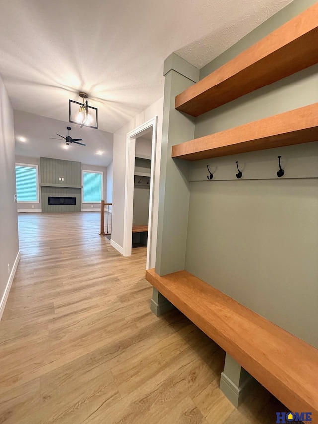 mudroom with a large fireplace, light wood-type flooring, baseboards, and ceiling fan