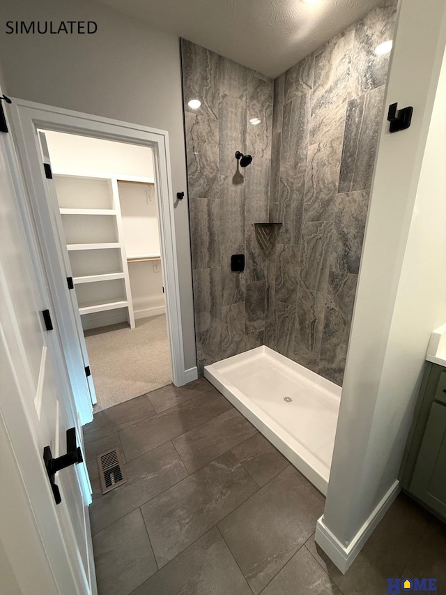 bathroom featuring visible vents, a tile shower, a walk in closet, and vanity