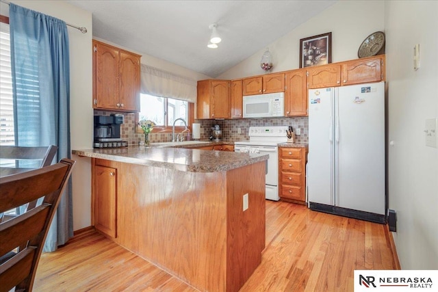 kitchen featuring white appliances, backsplash, a peninsula, and lofted ceiling