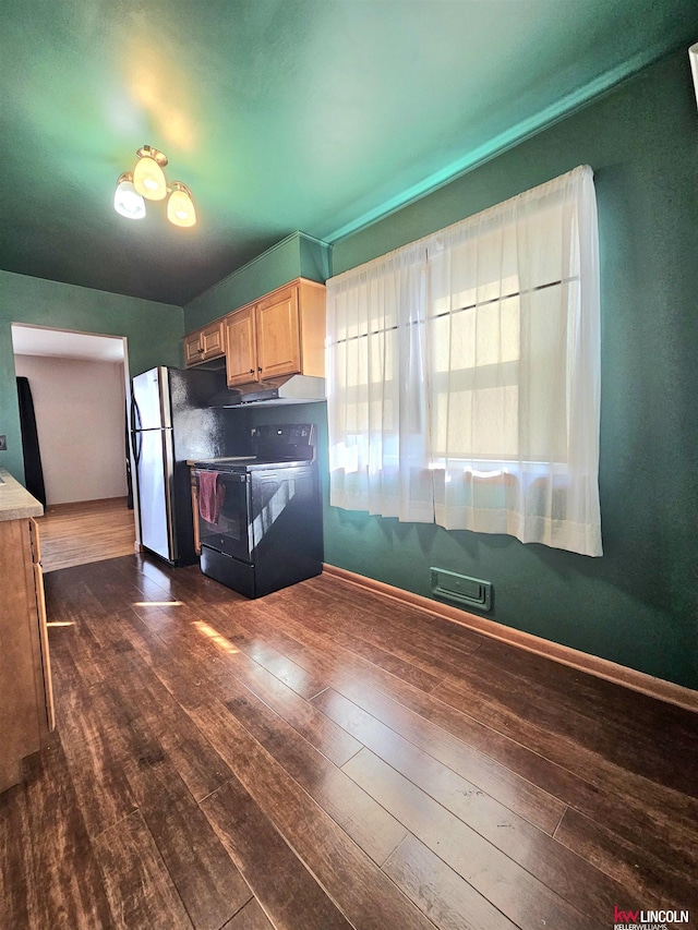 kitchen featuring dark wood finished floors, black range with electric stovetop, light brown cabinets, and freestanding refrigerator