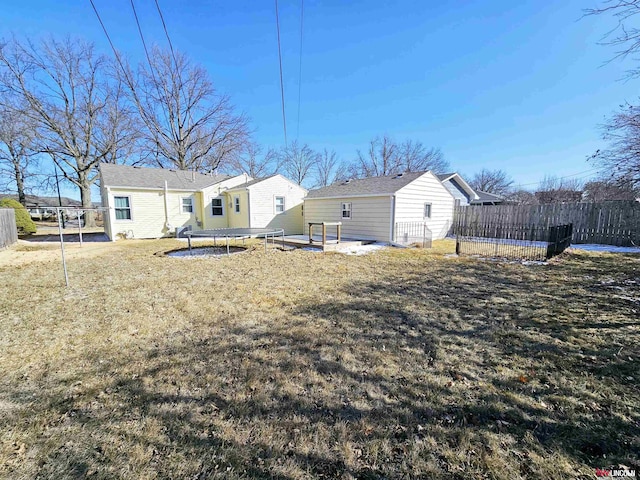 rear view of property with a yard, a trampoline, and fence