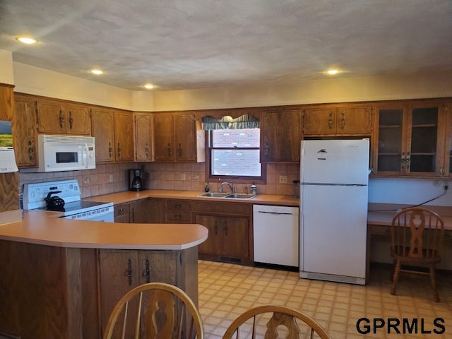 kitchen featuring light floors, light countertops, brown cabinets, white appliances, and a sink