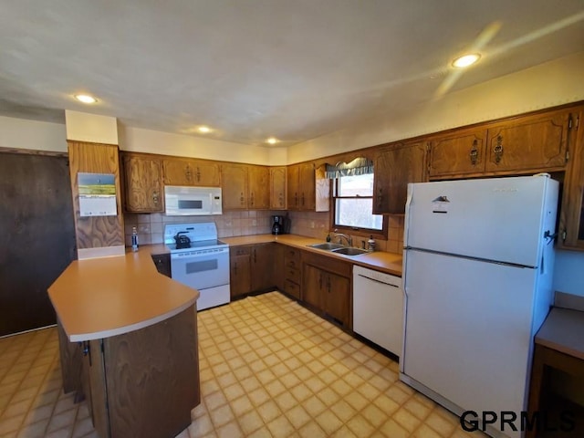 kitchen featuring a sink, white appliances, a peninsula, brown cabinetry, and light countertops