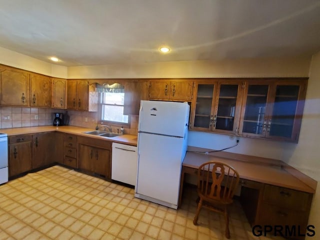 kitchen featuring brown cabinets, a sink, backsplash, white appliances, and light countertops