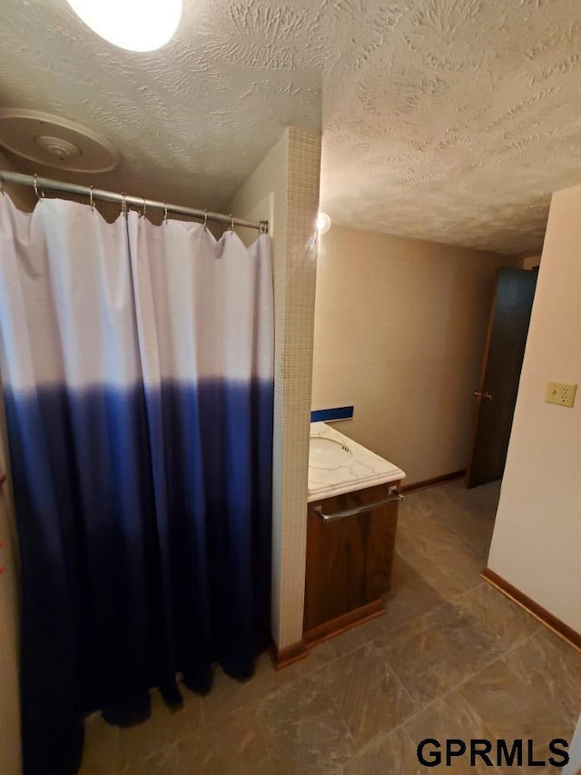 bathroom featuring a textured ceiling, vanity, a shower with shower curtain, and baseboards