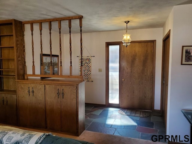 foyer featuring baseboards, stone tile floors, and a chandelier