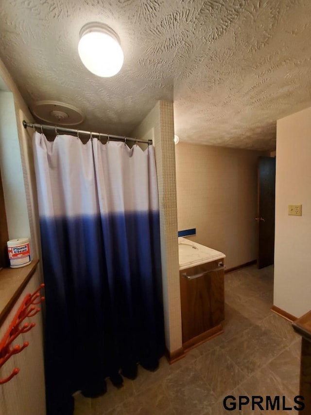 full bathroom featuring a shower with shower curtain, baseboards, a textured ceiling, and vanity