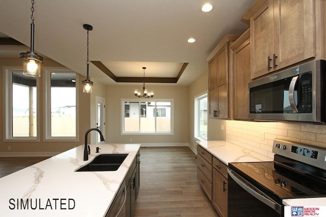 kitchen featuring light stone counters, a tray ceiling, a sink, decorative backsplash, and stainless steel appliances