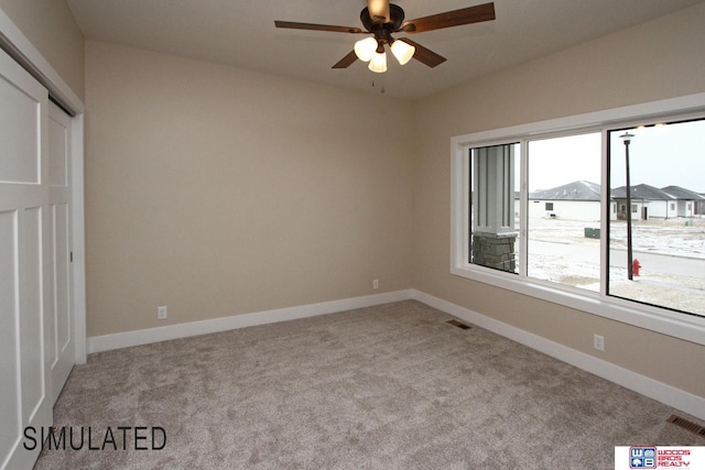 carpeted spare room featuring baseboards, visible vents, and ceiling fan