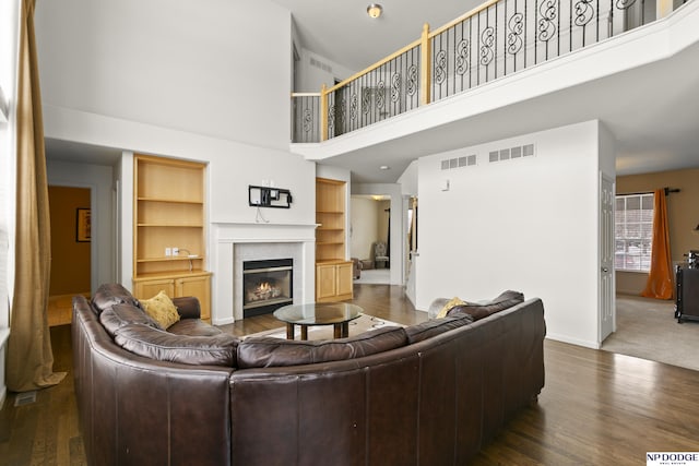 living room with visible vents, wood finished floors, a high ceiling, and a glass covered fireplace