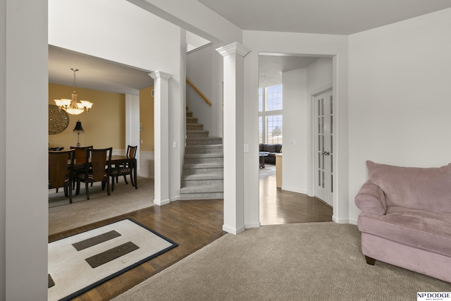 living area with dark wood-type flooring, stairs, an inviting chandelier, ornate columns, and dark colored carpet