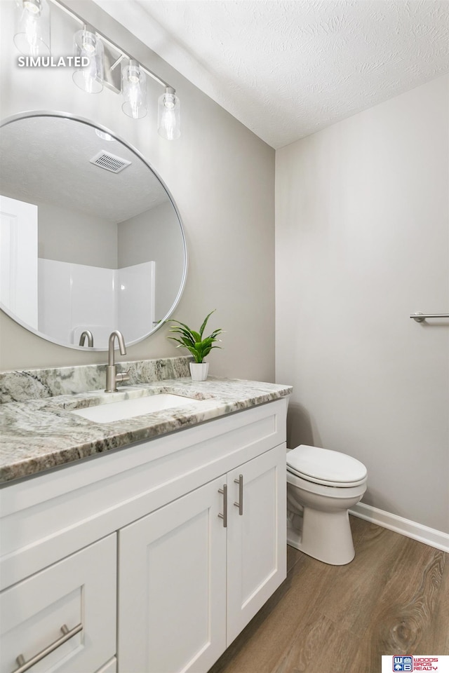 bathroom featuring visible vents, toilet, vanity, wood finished floors, and a textured ceiling