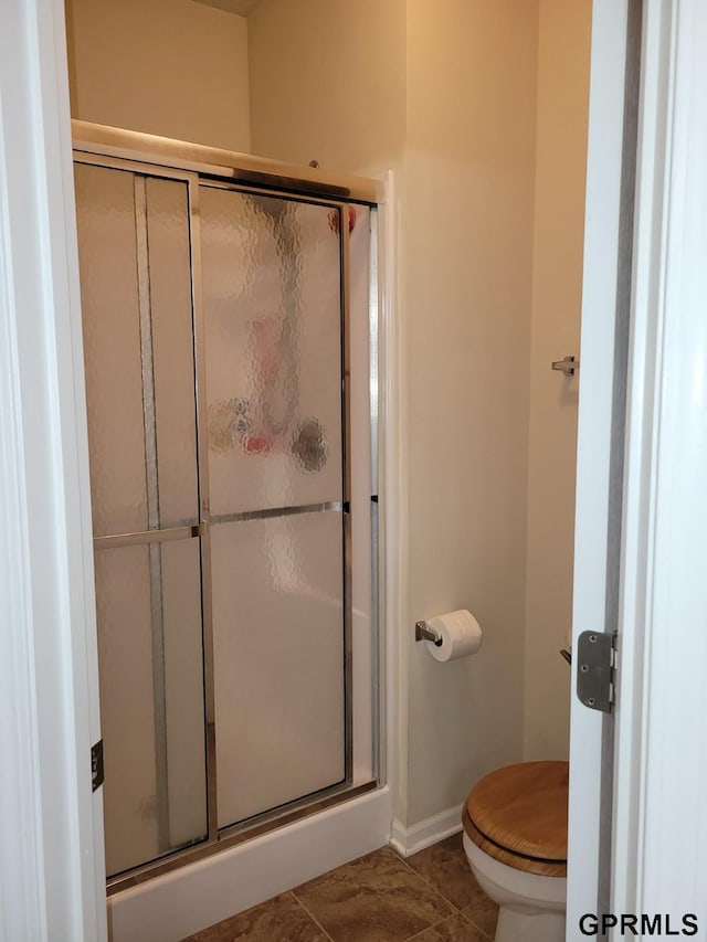 bathroom featuring tile patterned flooring, toilet, baseboards, and a stall shower