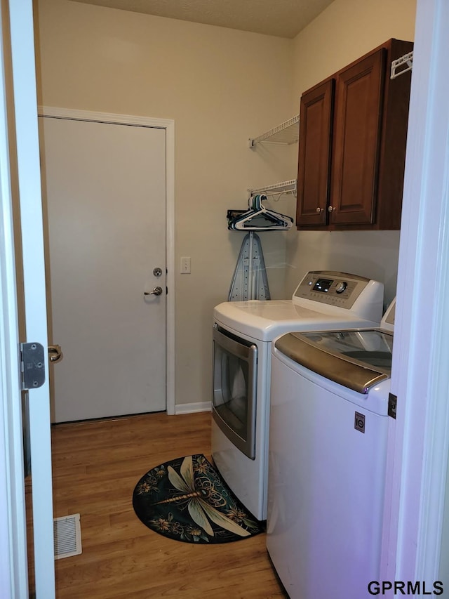 clothes washing area featuring visible vents, cabinet space, wood finished floors, and washer and clothes dryer