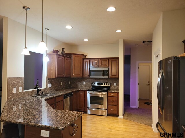 kitchen featuring a peninsula, a sink, hanging light fixtures, light wood-style floors, and appliances with stainless steel finishes