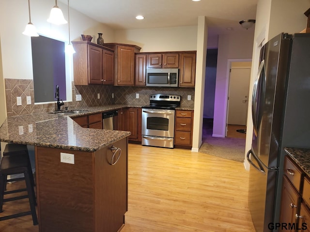 kitchen with light wood-type flooring, a peninsula, a sink, stainless steel appliances, and tasteful backsplash