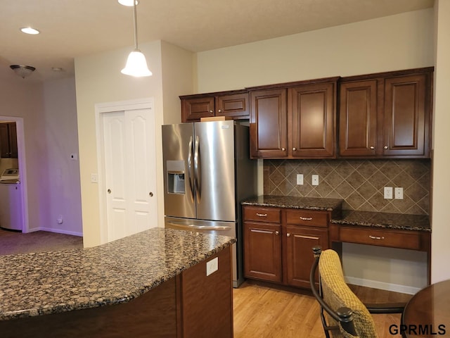 kitchen featuring backsplash, dark stone counters, washer / dryer, light wood-style flooring, and stainless steel refrigerator with ice dispenser