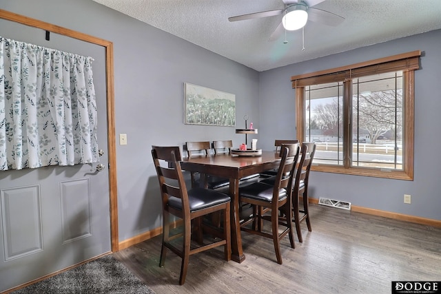 dining area with a ceiling fan, baseboards, wood finished floors, visible vents, and a textured ceiling