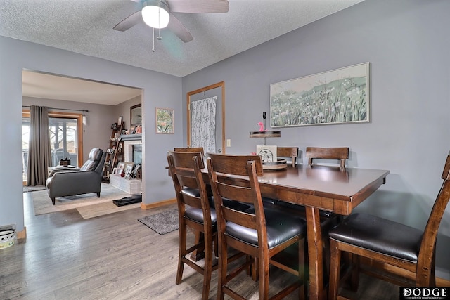 dining area featuring a fireplace with raised hearth, a ceiling fan, a textured ceiling, wood finished floors, and baseboards