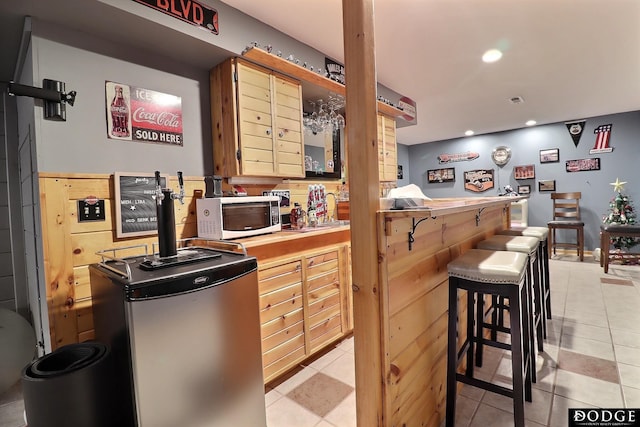 kitchen featuring white microwave, light tile patterned flooring, recessed lighting, freestanding refrigerator, and a kitchen bar