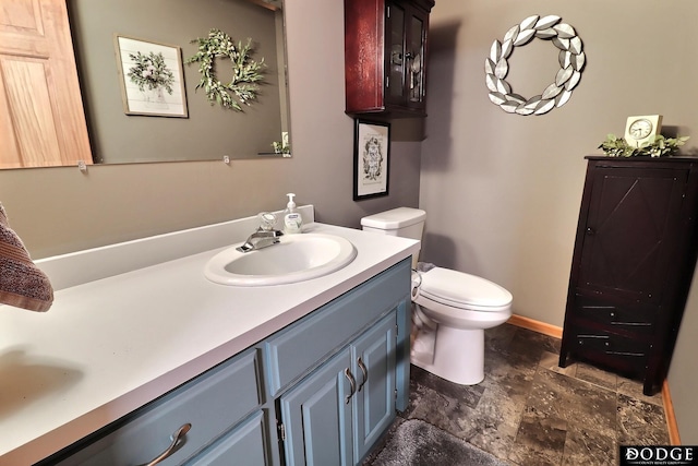 bathroom featuring stone finish flooring, toilet, vanity, and baseboards