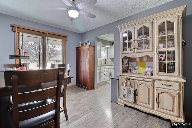 dining area featuring baseboards, a textured ceiling, a ceiling fan, and light wood-style floors