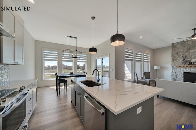 kitchen featuring a stone fireplace, appliances with stainless steel finishes, light wood-type flooring, and a sink