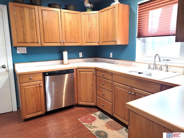 kitchen featuring light countertops, stainless steel dishwasher, wood finished floors, brown cabinetry, and a sink