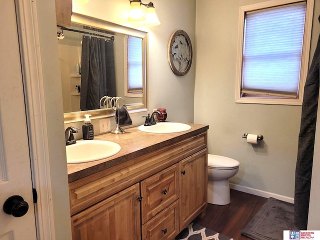 bathroom featuring double vanity, wood finished floors, toilet, and a sink