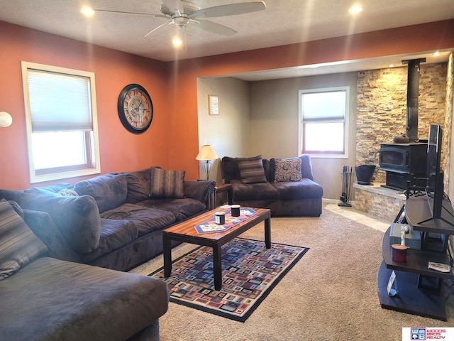 carpeted living room with a wood stove and a ceiling fan