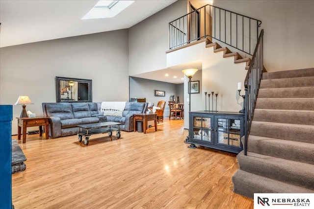 living room with high vaulted ceiling, a skylight, stairs, and wood finished floors