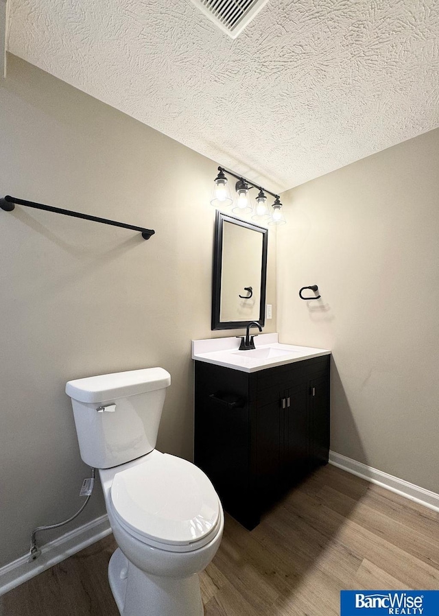 half bath featuring toilet, vanity, baseboards, and wood finished floors