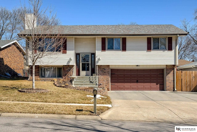 bi-level home with fence, driveway, a chimney, a garage, and brick siding