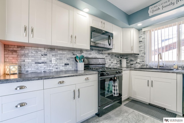 kitchen featuring black gas range oven, white cabinetry, tasteful backsplash, and a sink